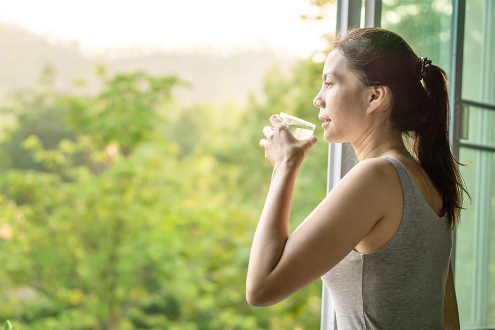 Woman drinking a glass of water by an open window