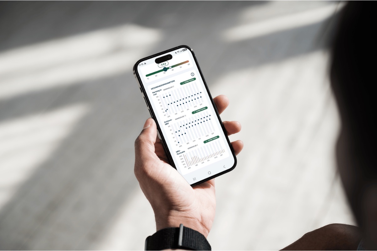 Iemand houdt een telefoon vast met de gezondheidsparameters van FibriCheck open, met grafieken van de hartslag in rust, ochtend-HRV en HRV-fluctuatie over enkele maanden, telkens met het label verbetering.