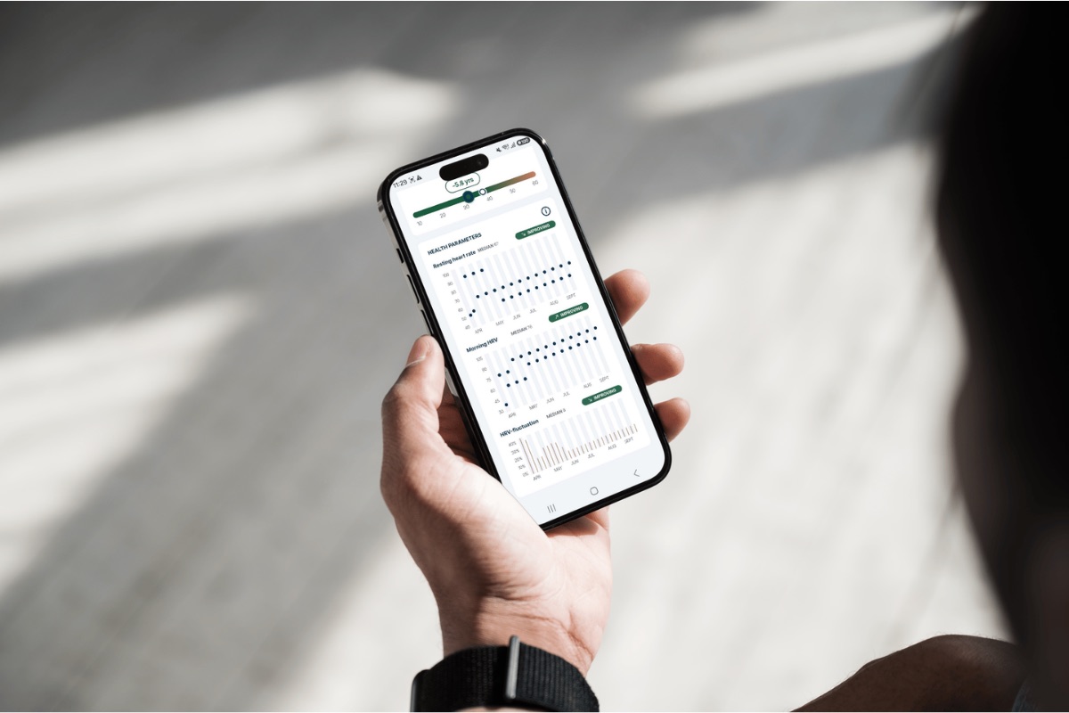 Someone holding a phone with the FibriCheck health parameters open, showing resting heart rate, morning HRV and HRV-fluctuation charts over several months, each labeled improving.